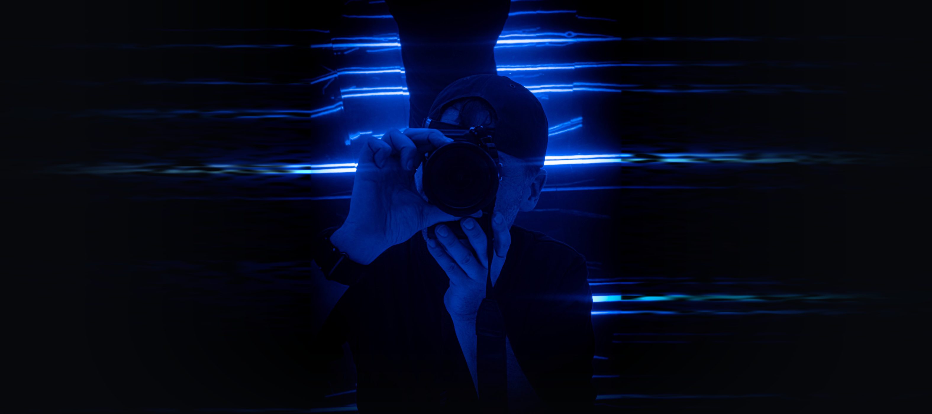 Alexander Siering fotografiert sich selbst mit der Kamera vor blauen Neonlinien, die links und rechts ins Dunkel auslaufen